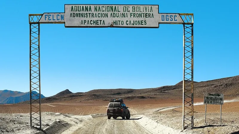 Portal fronterizo "Aduana Nacional de Bolivia – Apacheta Hito Cajones" con un vehículo 4x4 cruzando en paisaje desértico.