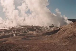 Campo geotérmico Sol de Mañana con géiseres emitiendo vapor sobre un paisaje árido y montañoso bajo cielo nublado.