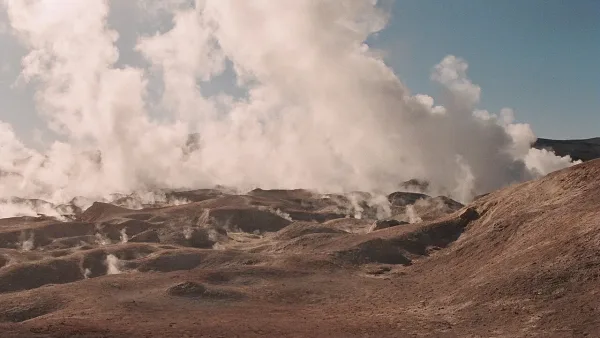 Campo geotérmico Sol de Mañana con géiseres emitiendo vapor sobre un paisaje árido y montañoso bajo cielo nublado.