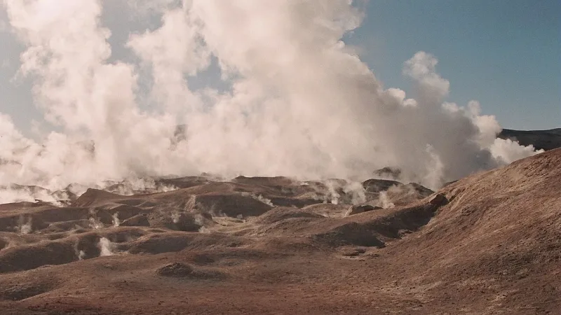 Campo geotérmico Sol de Mañana con géiseres emitiendo vapor sobre un paisaje árido y montañoso bajo cielo nublado.