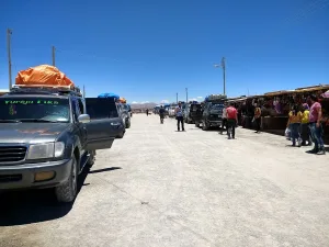 Camionetas 4x4 estacionadas frente al mercado de artesanías de Colchani, con turistas caminando bajo cielo despejado.