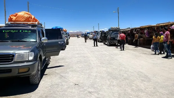 4WD vehicles parked along a dusty road beside the Colchani artisan market stalls under a clear blue sky