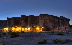 Pousada Mallku Cueva iluminada ao entardecer, encostada a grandes formações rochosas no deserto andino