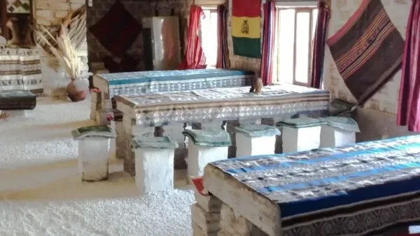 Interior de hotel de sal en el Salar de Uyuni con mesas y sillas de sal, bandera boliviana y textiles andinos.