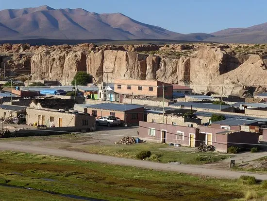 Pequeño pueblo altiplánico con edificios de adobe frente a formaciones rocosas y montañas áridas al fondo